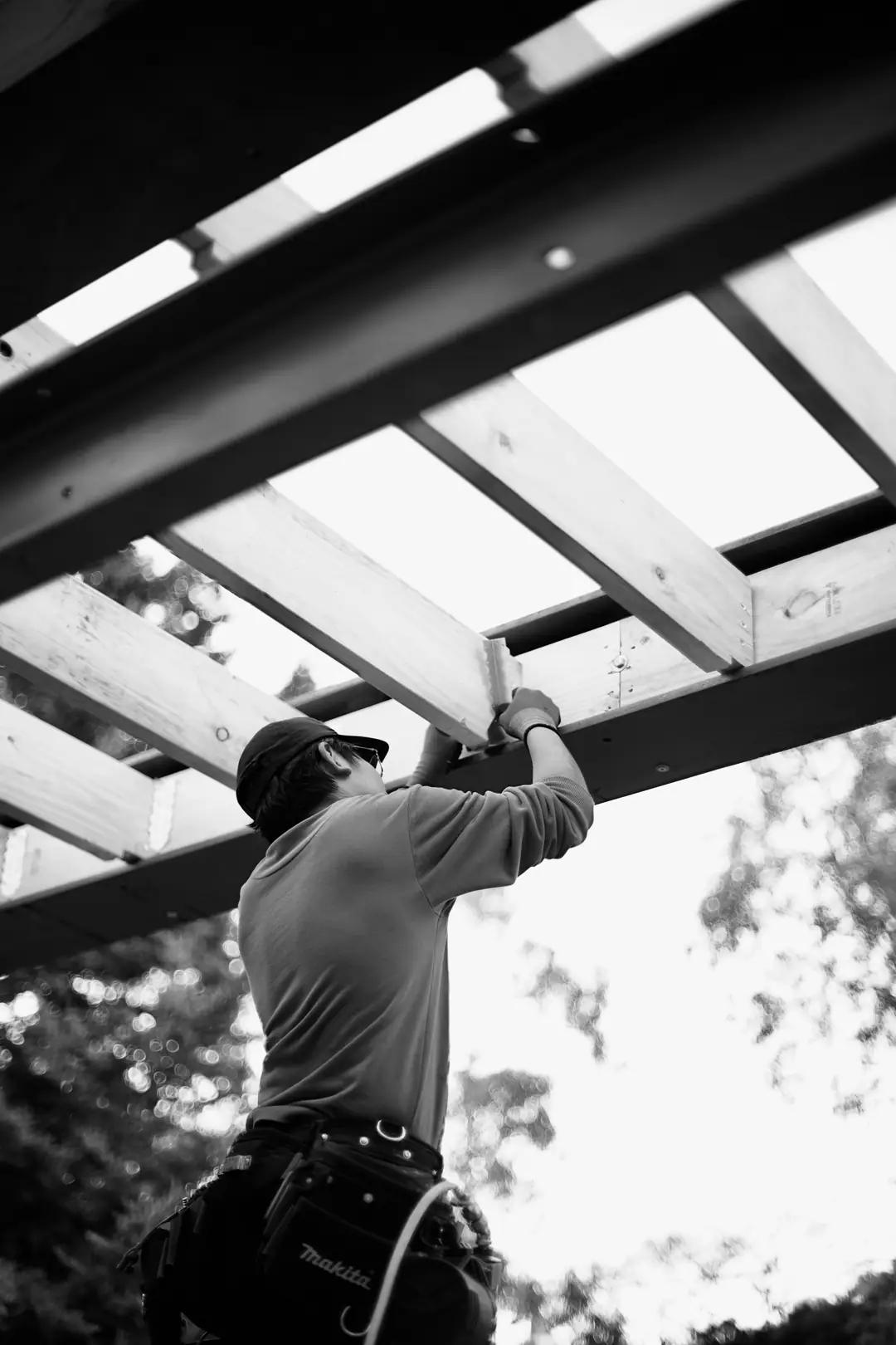 Carpenter fixing a timber roof member, photographed from below against the sky